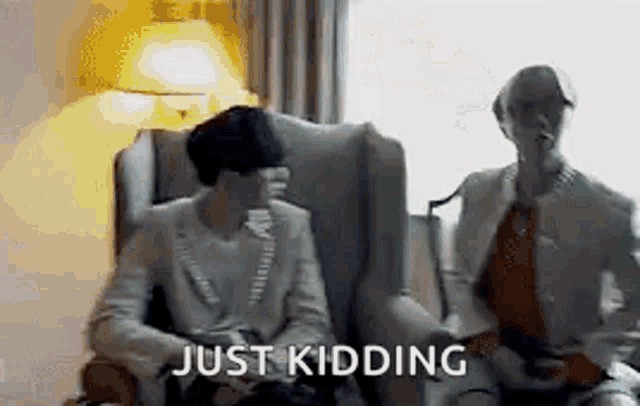 a man and a woman are sitting in chairs in a room with the words `` just kidding '' .