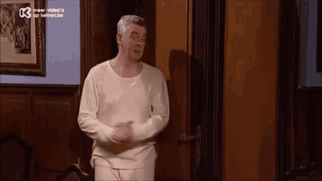 a man in a white shirt and underwear is standing in a room .