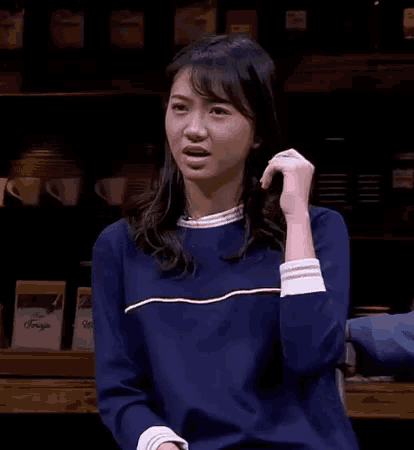 a woman in a blue sweater is making a funny face while standing in front of a counter .