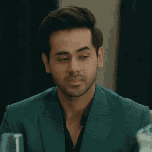 a man with his eyes closed is wearing a green suit and black shirt