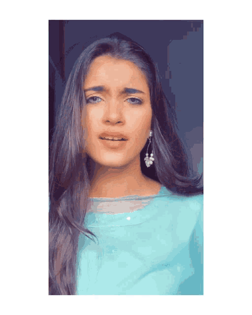 a woman wearing a light blue top and earrings looks at the camera