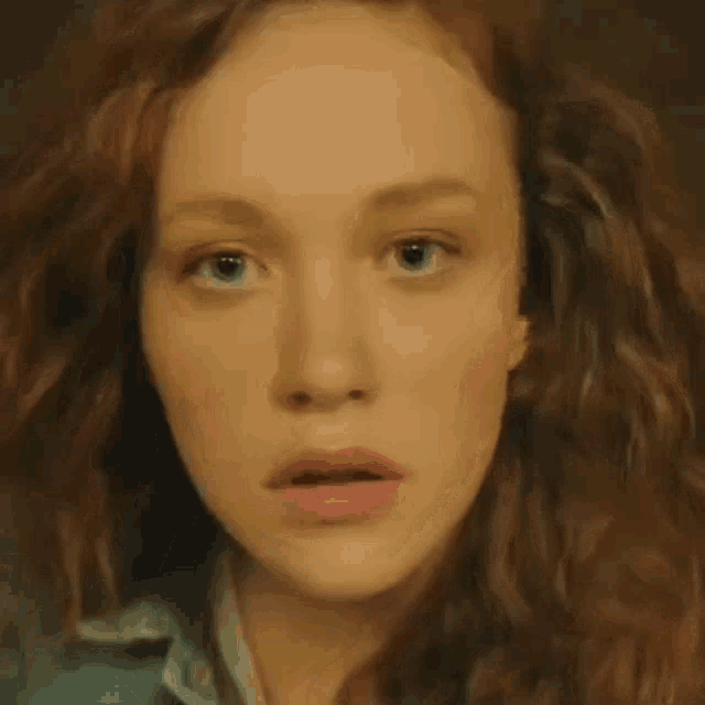 a close up of a woman 's face with red curly hair and blue eyes .