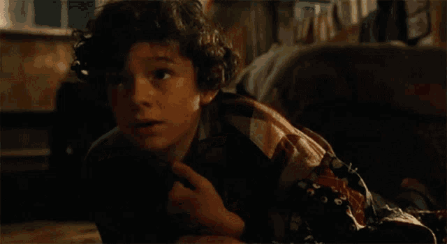 a young boy with curly hair is laying on the floor under a blanket