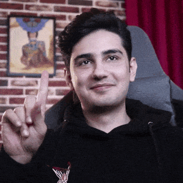 a man wearing a black hoodie is pointing up with his finger