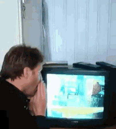a man wipes his face while watching a television