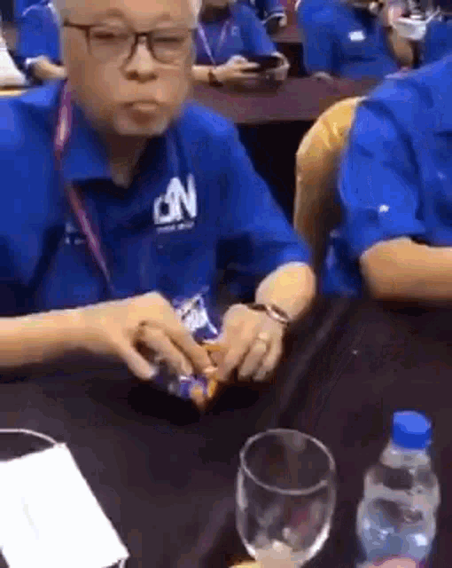 a man in a blue shirt is sitting at a table with a glass of water .