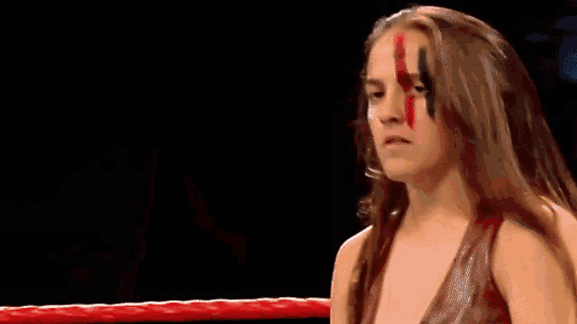 a woman with blood on her face is standing in a ring .