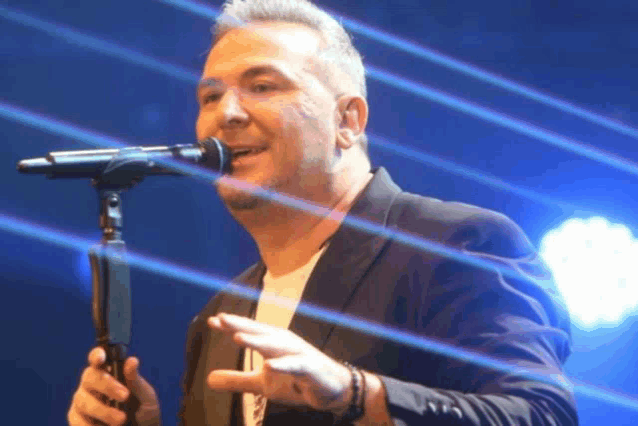 a man singing into a microphone with a blue background
