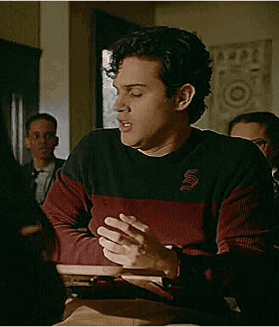 a young man is sitting at a desk in a classroom talking to someone .