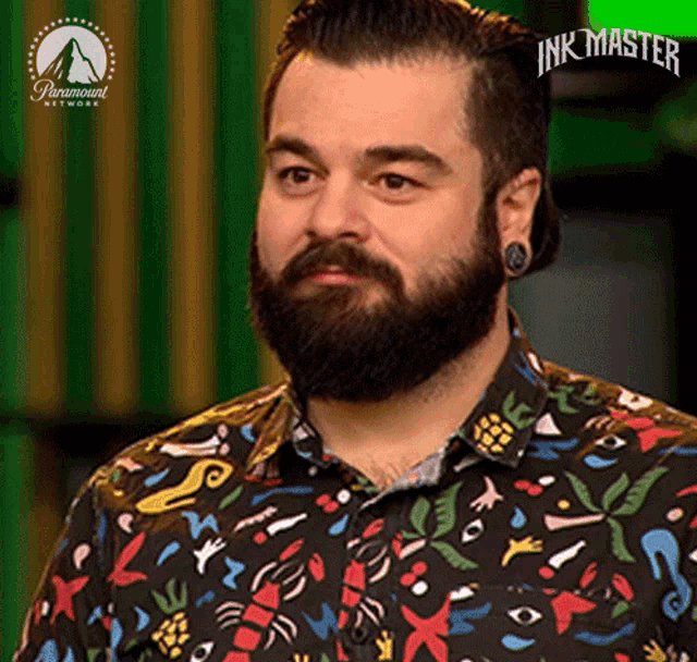 a man with a beard and piercings is wearing a colorful shirt and looking at the camera .