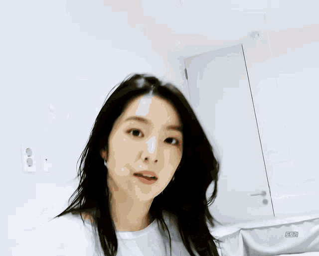a woman with long black hair is wearing a white t-shirt and looking at the camera .