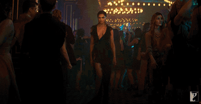 a woman in a black dress is walking through a crowd of people in a dark room