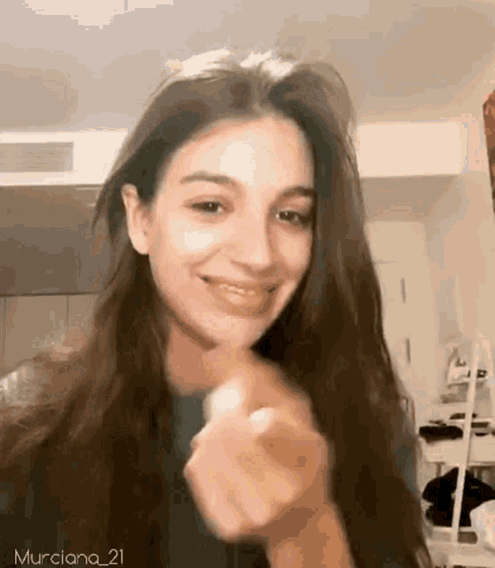 a woman with long hair is smiling and making a heart shape with her hand .