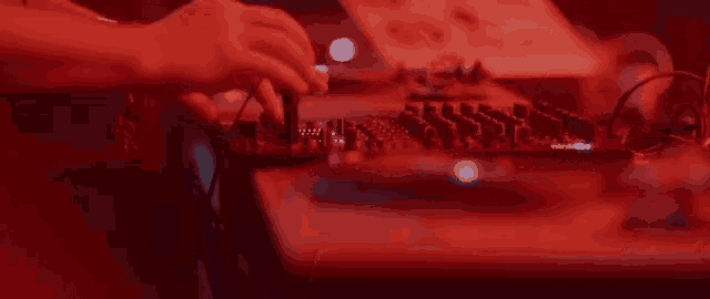 a dj is playing music on a mixer in a dark room with red lights .