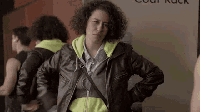 a woman wearing a leather jacket and a neon hoodie is standing in front of a mirror .