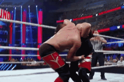 two men are wrestling in a ring with a referee in the background .