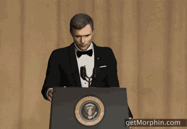 a man in a tuxedo stands at a podium with the seal of the president of the united states