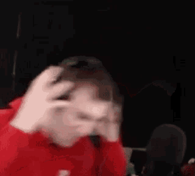 a blurry picture of a man in a red shirt standing in front of a microphone in a dark room .