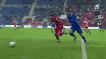 two soccer players are playing soccer on a field with a goal in the background .