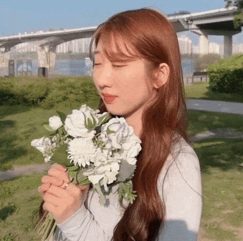 a woman smells a bouquet of white flowers in front of a bridge