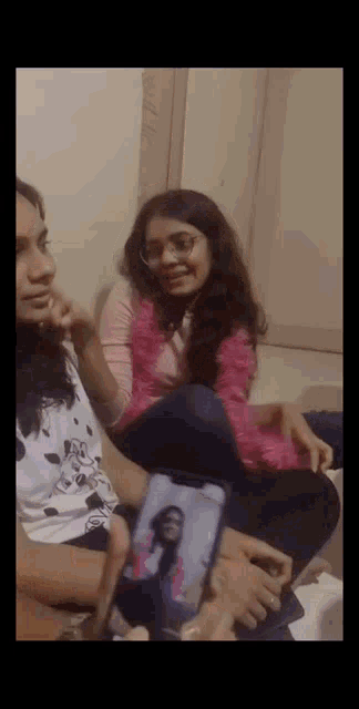 a group of girls are sitting on the floor looking at a phone .
