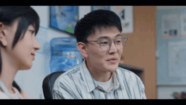 a man wearing glasses sits next to a woman in an office