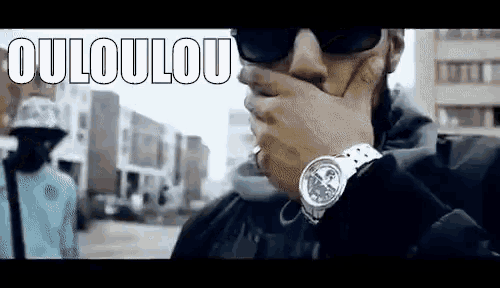 a man wearing sunglasses and a watch covering his mouth .