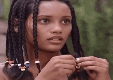 a young woman with braids and beads in her hair is looking at the camera .