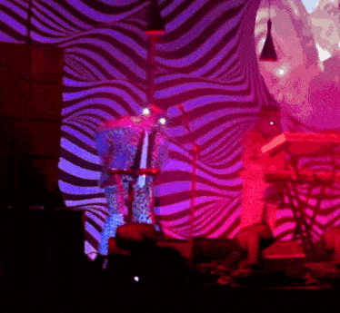 a man in a leopard print suit is playing a keyboard in front of a psychedelic backdrop