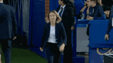 a woman wearing a white shirt and a black jacket is walking on a soccer field