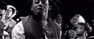 a black and white photo of a man with dreadlocks standing in front of a crowd .