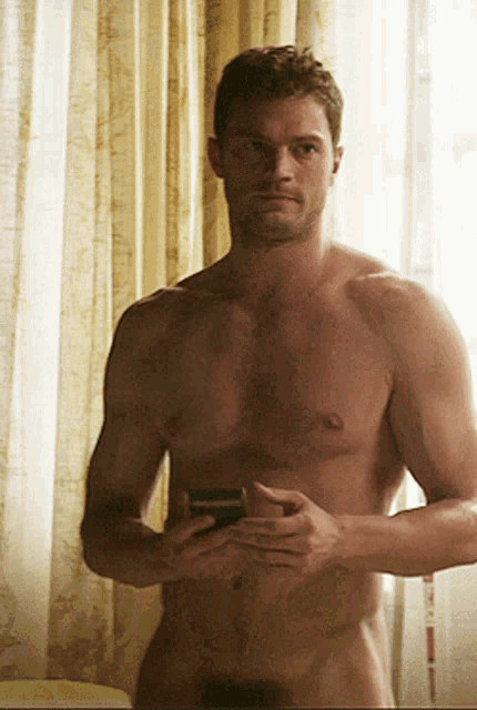 a shirtless man is standing in front of a window