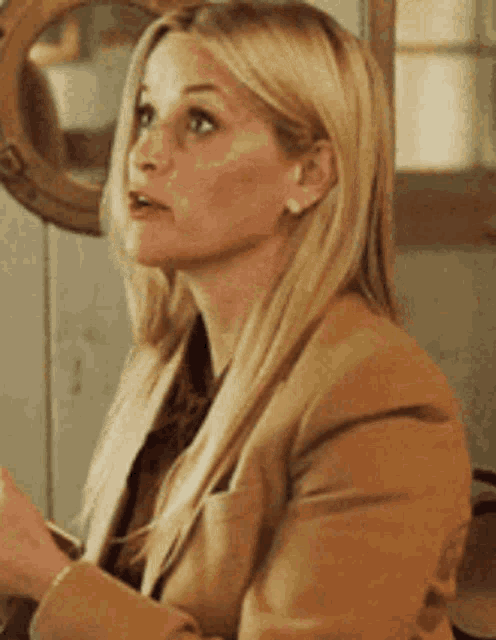 a woman in a tan jacket is sitting in front of a mirror looking up .