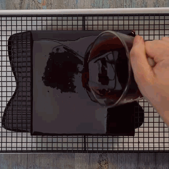 a person pouring chocolate sauce into a pan on a wire rack