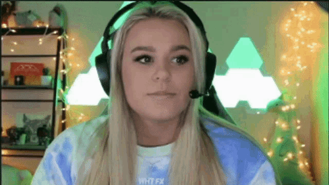 a woman wearing headphones and a tie dye shirt with the word fx on it looks at the camera
