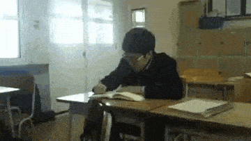 a young man is sitting at a desk in a classroom .