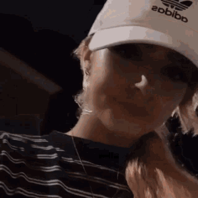 a woman wearing a white adidas hat and a black and white striped shirt .