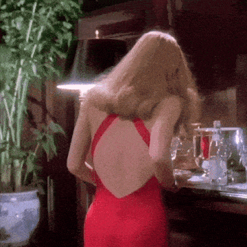 a woman in a red dress with a low back is standing in front of a lamp