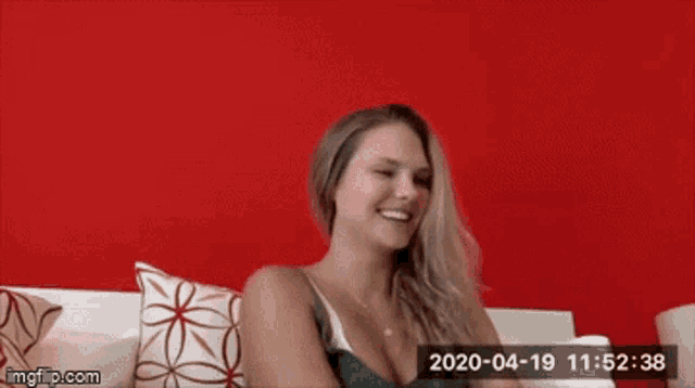 a woman is sitting on a couch with a red wall behind her ..