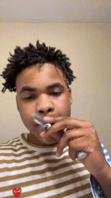 a young man in a striped shirt is brushing his teeth with a toothbrush