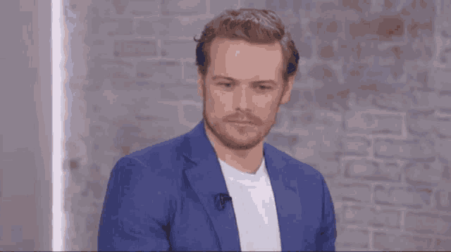 a man in a blue suit and white shirt is standing in front of a brick wall