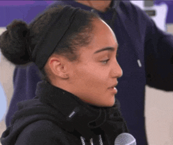 a woman wearing a headband and a black hoodie is talking into a microphone ..