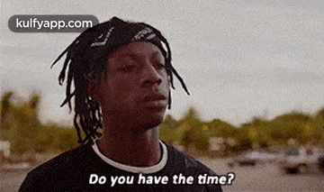 a man with dreadlocks is standing in a parking lot and asking do you have the time ?