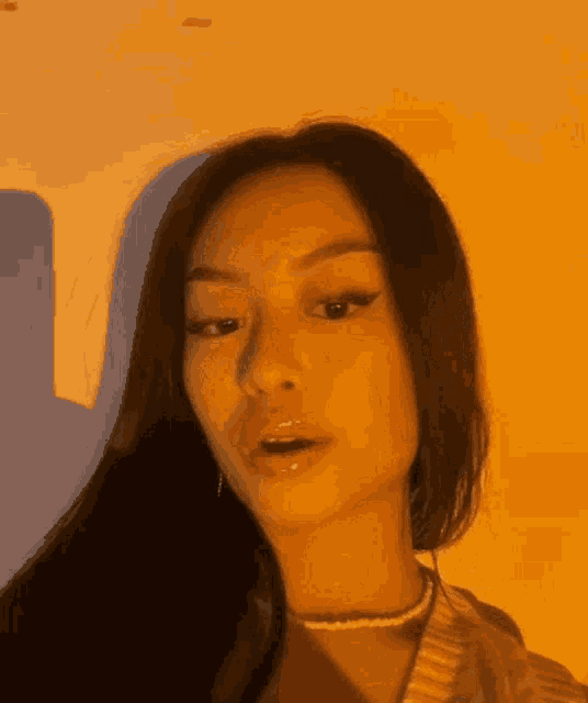 a close up of a woman 's face in front of a wall with an orange light behind her .