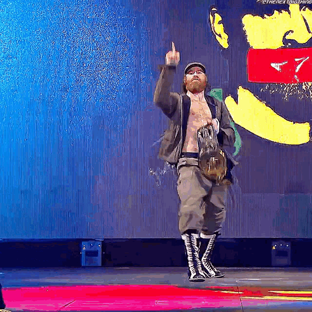 a man with a beard is standing on a stage giving a middle finger .