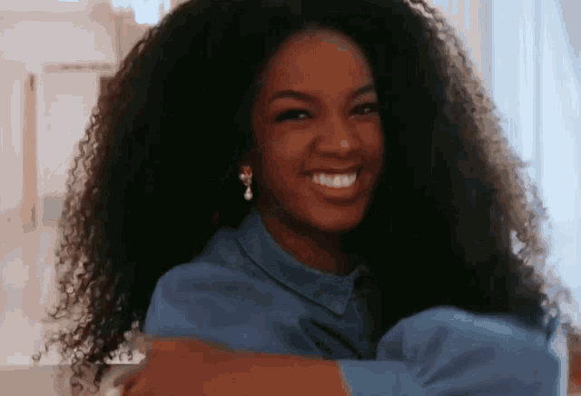 a woman with curly hair wearing a blue shirt and earrings smiles for the camera