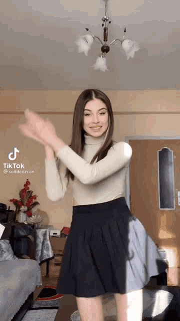 a woman in a skirt is dancing in a living room with her hands in the air .