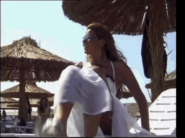 a woman in a white dress is sitting under an umbrella on a beach