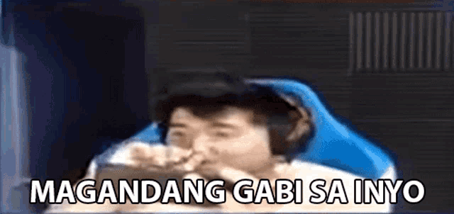 a man wearing headphones is sitting in front of a computer screen with the words magandang gabi sainyo written on it .
