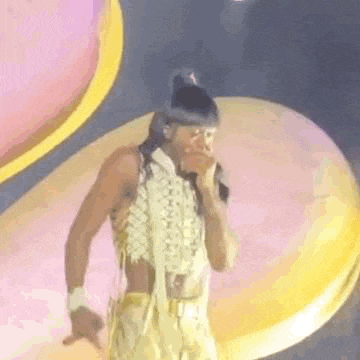 a man is singing into a microphone on a stage while wearing a gold outfit .